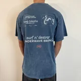 Remera azul con efecto gastado, corte holgado y estampado en el frente y la espalda con motivos surferos y el texto "Surf n' Destroy".