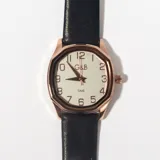 Reloj de pulsera con caja dorada de forma octogonal y esfera blanca con números arábigos. Correa de cuero negra.