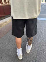 Bermuda de jean negra gastada, corte amplio a la rodilla.