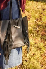 Bolso maxi negro de cuero con flecos y botón de guampa. Tiene bolsillo interior y cierre metálico.