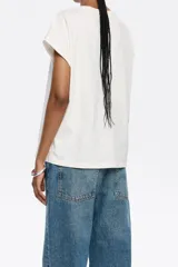 Camiseta blanca de algodón con corte recto, cuello redondo y mangas cortas tipo murciélago. Estampado frontal con el logo de la marca Bimba y Lola en color beige.