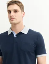 Remera polo blanca de piqué con cuello y puños en azul marino. Tiene tapeta de dos botones y bolsillo de parche en el pecho.