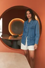 Campera de denim celeste con corte recto, cuello camisero, cierre frontal con botones metálicos, bolsillos con solapa y volados en el frente.