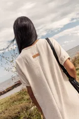 Vestido midi color crema, de corte recto y mangas cortas con puños elásticos. Presenta aberturas laterales en el ruedo.
