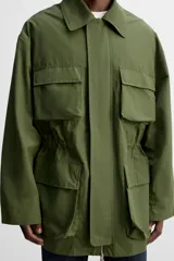 Parka verde militar de tejido técnico ligero, corte relaxed fit, cuello solapa y manga larga. Tiene cuatro bolsillos de plastrón con solapa en el delantero, cintura ajustable en el interior y cierre frontal con cremallera oculta por solapa con botones a presión.