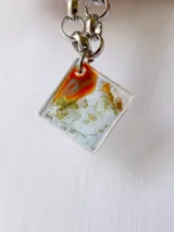 Pulsera con cadena de eslabones plateados y dije de resina transparente con detalles en amarillo, blanco, verde y dorado.