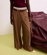 Pantalón de vestir marrón con finas rayas verticales blancas, de corte recto y tiro alto. Se ajusta a la cintura con cinturón de cuero marrón.