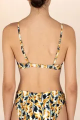Top de bikini tipo triángulo con estampado de hojas en tonos mostaza, negro y blanco. Presenta tirantes delgados ajustables y un accesorio metálico dorado con forma de hoja en el centro del busto.