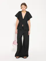 Pantalón negro de lanita viscosa, corte wide leg con gran caída y movimiento. Acceso mediante cierre metálico, gancho pantalonero y botón interno. Incluye lazo en cintura con media caña marcaria de níquel.