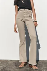 Pantalón de jean color beige, de tiro alto, corte ajustado en la cadera y muslos, y acampanado desde la rodilla. Tiene cinco bolsillos y cierre frontal con cremallera y botón.