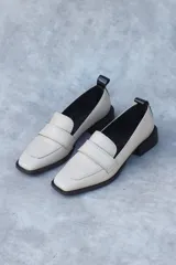 Zapato tipo mocasín de cuero con tacón bajo y punta cuadrada, diseñado con suela lisa que sobresale levemente y tirador acharolado en la parte trasera.
