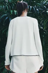 Chaqueta blanca de punto con cuello redondo y manga larga. Tiene vivos negros en el cuello, el borde frontal y los puños. Se cierra con botones en el frente.