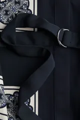 Vestido camisero de manga larga, con cuello camisero y cierre frontal de botones ocultos. Presenta un estampado tipo pañuelo en tonos blanco, azul marino y azul claro, y se ajusta a la cintura con un cinturón extraíble con argollas metálicas.