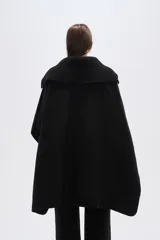 Poncho negro de tejido grueso, con cuello alto de punto acanalado y cierre frontal con cremallera.