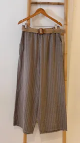 Pantalón de lino azul marino con rayas verticales blancas, corte palazzo, cintura alta con elástico y cinturón de raffia con hebilla redonda.