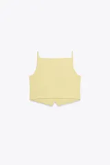 Chaleco amarillo pálido con cuello cuadrado, tirantes finos, falsos bolsillos de vivo y cierre frontal con botones.