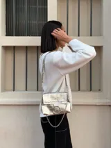 Cartera bandolera negra de ecocuero con textura arrugada, tachas plateadas, cadena decorativa y aro metálico.