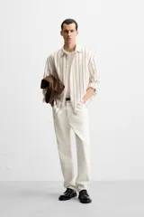 Camisa de hombre regular fit, color blanco con rayas verticales negras, cuello solapa, manga larga con puños abotonados y cierre frontal con botones.