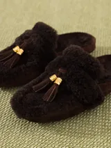 Mocasín marrón de cuero vacuno y gamulán de oveja, con borlas en el empeine y terminales doradas. Suela de goma.