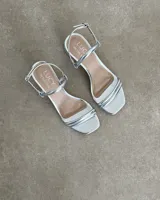 Sandalias bajas blancas con tiras tubulares plateadas y hebilla ajustable en el tobillo.