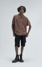Camisa de tejido de punto color café, manga corta y cuello polo con botones frontales. Presenta un patrón calado de espiga o chevron.