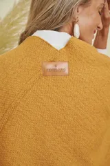 Ruana tejida color mostaza con terminación en flecos de lana y espalda en forma de V.