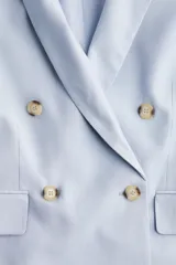 Blazer celeste de doble botonadura con solapas de muesca, hombreras y bolsillos delanteros ribeteados con solapa.