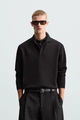 Polo de manga larga color negro, tejido en punto de algodón, corte relaxed fit, cuello solapa y cierre frontal con botonadura.