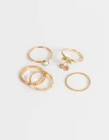 Set de 5 anillos dorados de metal con diferentes diseños: uno torzado, uno con strass, uno con dije de cerezas con strass de colores, uno con strass engarzado y uno liso.