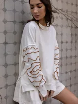 Buzo blanco de jogging sin friza, con bordado floral marrón en las mangas.