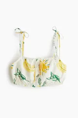 Top corto con estampado de bananas y hojas verdes, breteles finos con lazos ajustables, escote recto con cordón ajustable y elástico en el bajo.