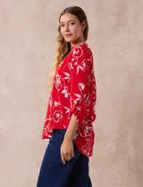 Blusa de gasa roja con estampado floral blanco, cuello a la base con escote en V y mangas 3/4 regulables con presilla y botón.