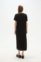 Vestido largo negro de manga corta, corte recto y holgado, con escote en V y un detalle de adorno tipo broche en el centro del escote.