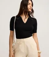 Blusa negra de punto con cuello polo, escote en V y mangas cortas. Detalle de mini perlas aplicadas en el cuello.