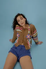 Saco de crochet color marrón con diseño de patchwork con motivos florales en tonos rosa, celeste y amarillo. Tiene cuello camisero, cierre frontal con botones y mangas largas. Tejido en algodón.