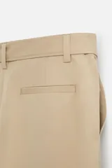 Pantalón negro de corte ancho con cinturón de tela con hebilla metálica y pliegues frontales.