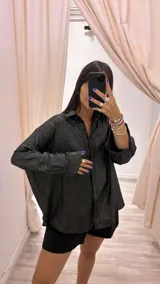Camisa negra con finas rayas verticales plateadas de lurex, corte holgado, cuello camisero y mangas largas con puños abotonados.