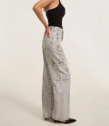 Pantalón de mujer wide leg en jeans de algodón, color celeste claro con efecto lavado. Presenta talle alto con trabillas, cierre de botón y cremallera, bolsillos delanteros y traseros, un bolsillo cargo lateral y un recorte transversal en la pierna.