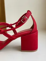 Sandalias rojas de cuero, con tiras finas con nudos en el empeine y pulsera con hebilla en el tobillo. Taco cuadrado de 7 cm.