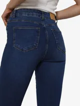 Pantalón de jean azul oscuro, de tiro alto y corte ajustado en la cadera y muslos, con bota acampanada. Cierre frontal con botón y cremallera.