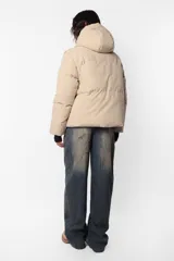 Campera puffer beige de corte oversize, confeccionada en textil impermeable. Cuenta con capucha forrada con tancas y elástico, cuello alto, cierre frontal con cartera y abrojo, bolsillos ribete con cierre, mangas desmontables con mitones y cintura ajustable con elástico y tancas. Incluye cinta gross estampada para transportarla al hombro y bolsillo interno con cierre invisible.