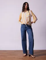 Blusa de gasa estampada a rayas verticales en tonos celeste, lila, naranja y marrón. Tiene cuello a la base con escote en V y botones. Delantera con bolsillo aplicado. Largo de manga regulable con presilla y botón. Terminación anudada opcional.