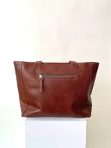 Cartera tipo tote de cuero graneado color negro, con textura uniforme y suave al tacto. Tiene manijas de 55 cm, bolsillo frontal con broche imantado, bolsillo trasero con cierre metálico, cierre principal metálico, forro interior y tres bolsillos internos (uno con cierre, uno plaqué y uno tipo sobre con solapa y botón).