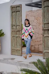 Sweater de punto color crudo con cuello redondo negro y bordados decorativos en forma geométrica en colores fucsia, verde y naranja. Tiene mangas largas con puños negros.