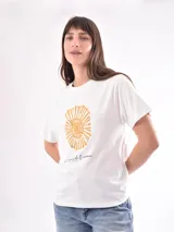 Remera blanca de algodón con cuello redondo y mangas cortas. Estampado frontal con diseño de concha marina en color ocre y texto manuscrito en negro.