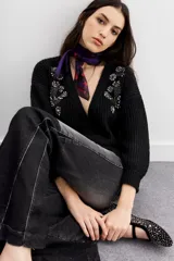 Cardigan negro de tejido de punto con ochos y terminaciones en punto rib. Presenta calce relajado, mangas largas y apliques bordados en piedras y canutillos en la parte superior del frente.