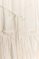Vestido largo color blanco roto o crema, con textura plisada o arrugada verticalmente. Presenta un cuello halter que se ata en la nuca y espalda descubierta.
