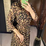 Vestido largo de playa con estampado animal print de leopardo en tonos marrones y negros. Tiene corte holgado, mangas largas y abertura frontal con lazo en la cintura.