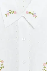 Camisa blanca de mangas cortas con bordado de flores rosas y celestes.