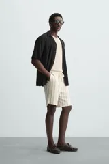 Camisa de calce relajado confeccionada en tejido fluido de mezcla de viscosa, color blanco. Presenta cuello bowling, manga corta, aberturas laterales en el bajo y cierre frontal con botones al tono.